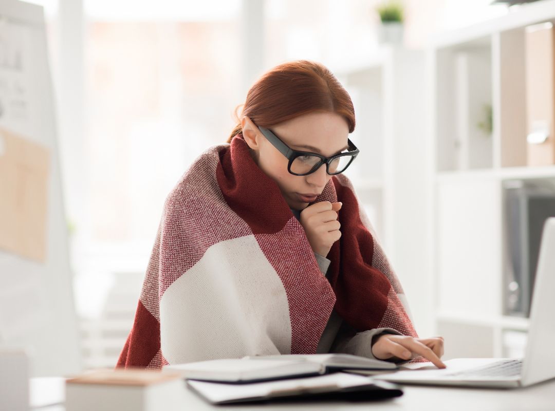 There is a woman with glasses with a blanket around her in an office space.